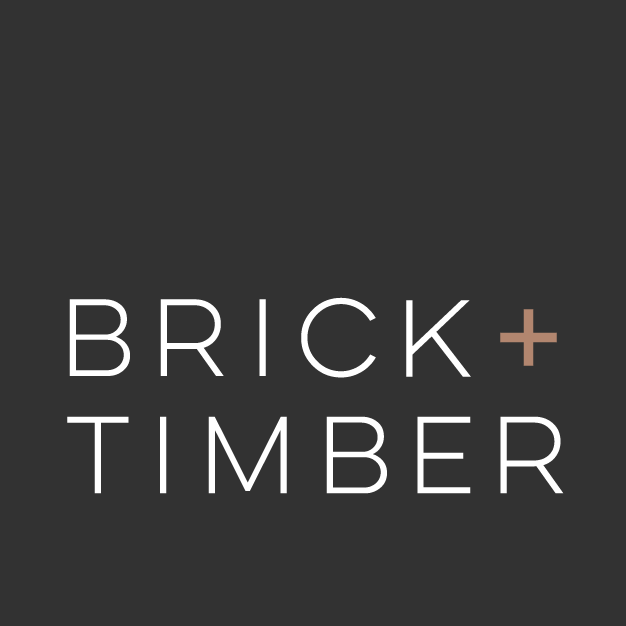 Logo of "Brick + Timber" a property management company in San Francisco, CA, displayed on a dark gray background. The "+" symbol is highlighted in a copper tone.